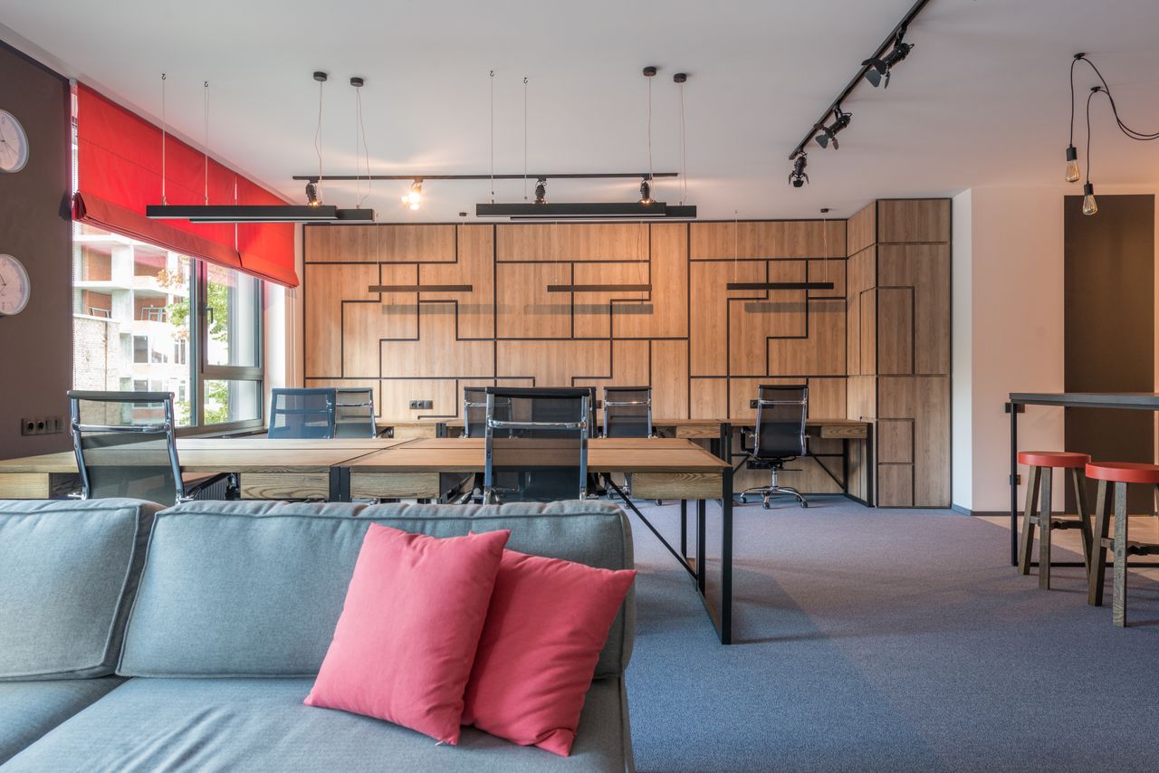services-03 Sofa with cushions against tables and armchairs under hanging lamps in contemporary office in daylight